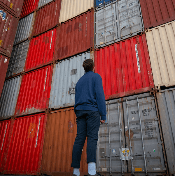 A man stands thoughtfully before shipping containers